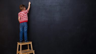 Back view of cute little kid boy writing with chalk